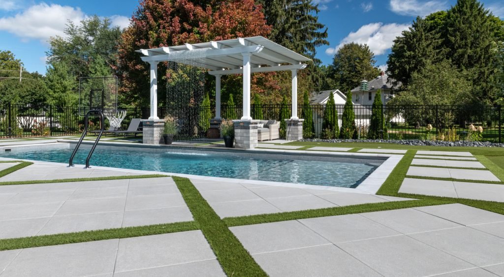 White gazebos with a fabric canopy sit poolside, offering shaded seating in a modern backyard oasis.