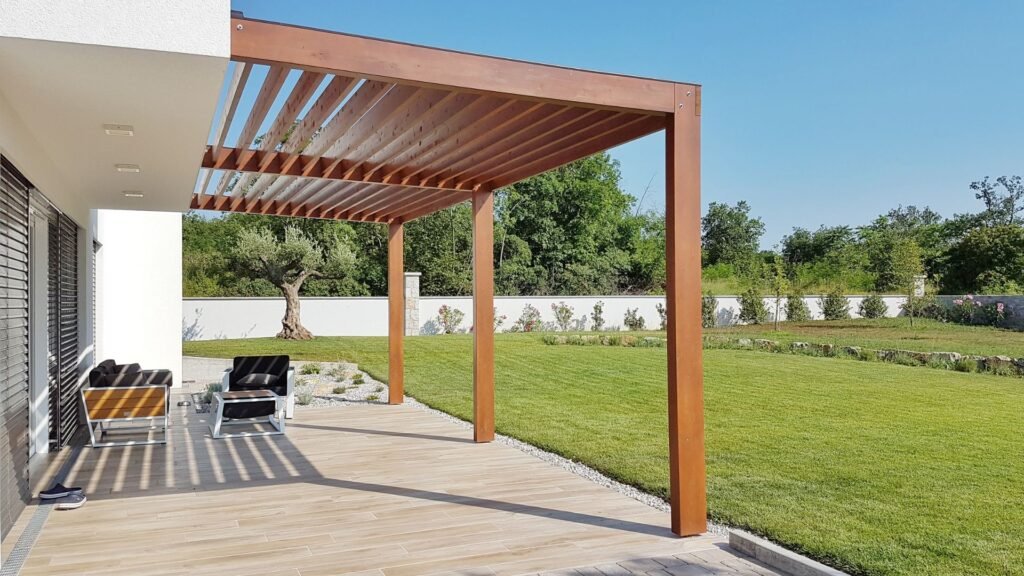 Elegant pergola with wooden beams complements tiled patio and peaceful backyard lawn with stone accents.