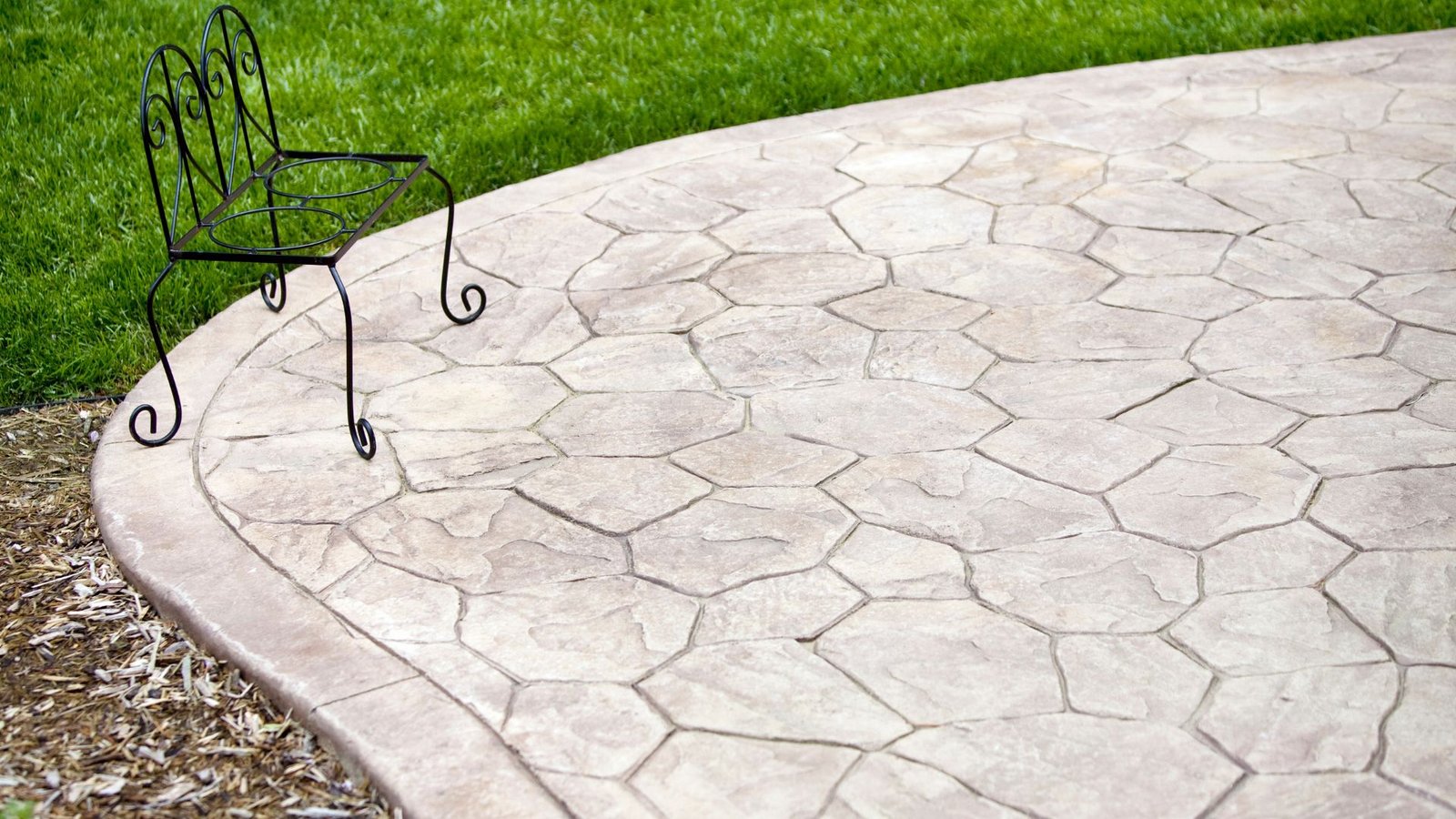 Custom-designed stamped concrete surface mimicking flagstone, installed next to vibrant grass and mulch bed.
