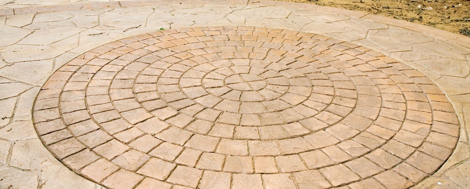 Detailed concentric concrete circle pattern in patio, blending geometric precision with natural stone-style background.